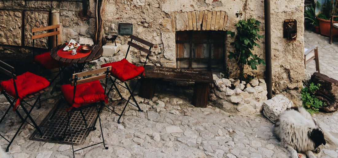 patio table and four chairs with red cushions on a cobblestone patio with a sleeping dog